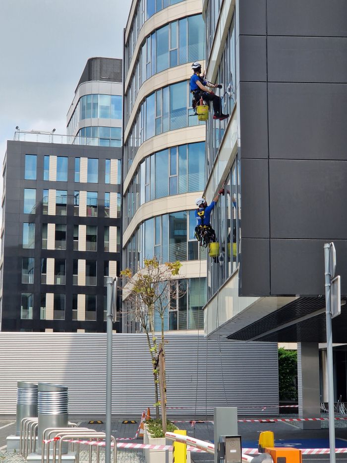 Deux ouvriers nettoient les vitres d’un immeuble de bureaux élevé dans un environnement urbain.
